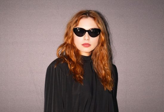 Poznata glumica odabrala je kreaciju s potpisom domaćeg brenda eNVy room, i to u klasičnoj crnoj nijansi koja je uvijek sinonim za eleganciju. Duga silueta haljine u potpunosti prati liniju tijela, ali na vrlo suptilan način – bez pretjeranog naglašavanja, već s dozom profinjene ležernosti. Puhasti, blago voluminozni rukavi donose dodatnu notu retro šarma, dok visoki struk s fokusom na detalj u vidu crvene satenske vrpce i ukrasne broševe unosi neočekivanu dozu glamura i boje. Najveći adut cijelog stylinga je upravo balans: dramatična crna haljina, kontrastni crveni akcent i odvažan izbor modnih dodataka u vidu crvenih cipela koji upotpunjuju vizualnu priču. Look je zaokružen diskretnim, ali upečatljivim makeupom te raskošnom kosom stiliziranom u mekanim valovima. Tamne naočale dale su cijeloj kombinaciji dojam hollywoodskog glamura i misterije. Judita je ovim pojavljivanjem pokazala da se ne boji modnih eksperimenata, ali uvijek bira rješenja koja naglašavaju njezinu osobnost i sofisticiranost. Ovaj outfit savršeno dokazuje da prava modna snaga leži u detalju – a Judita ga je pretvorila u svoj zaštitni znak večeri. Naš je zaključak jasan: Judita Franković Brdar i eNVy room stvorili su jedno od onih izdanja koje se pamti. Glumica se u ovom upečatljivom looku pojavila upravo na reviji modnog brenda eNVy room.